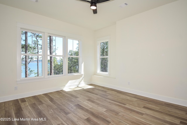 spare room featuring a ceiling fan, visible vents, baseboards, and wood finished floors