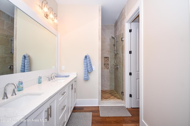 bathroom featuring a stall shower, baseboards, a sink, and wood finished floors