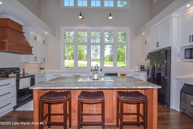 kitchen with a center island, custom range hood, white cabinetry, a towering ceiling, and black appliances