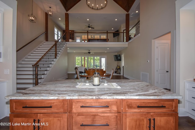 kitchen with light stone countertops, recessed lighting, ceiling fan with notable chandelier, open floor plan, and a towering ceiling