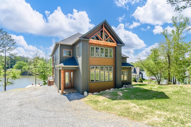 contemporary house with board and batten siding, roof with shingles, a water view, and a front yard