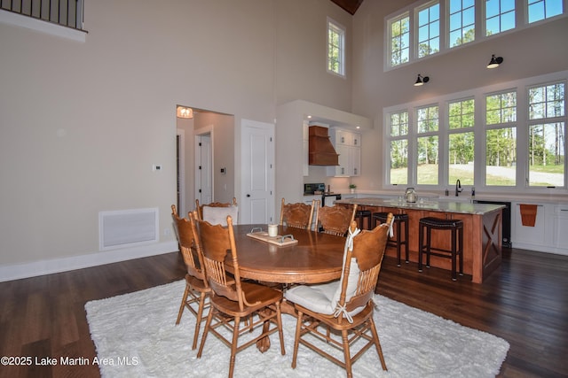 dining space with baseboards, dark wood-style flooring, visible vents, and a high ceiling