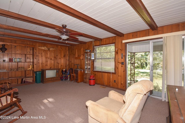 living room with beamed ceiling, ceiling fan, wood walls, and carpet floors