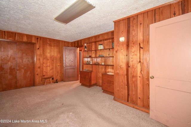 unfurnished room featuring wooden walls, light colored carpet, and a textured ceiling