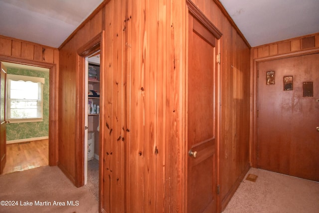 hallway featuring wood walls, crown molding, and light colored carpet