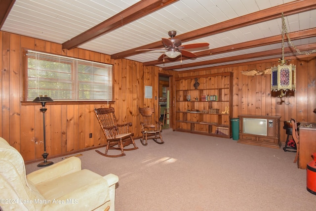 living area with carpet floors, wooden walls, beamed ceiling, and ceiling fan