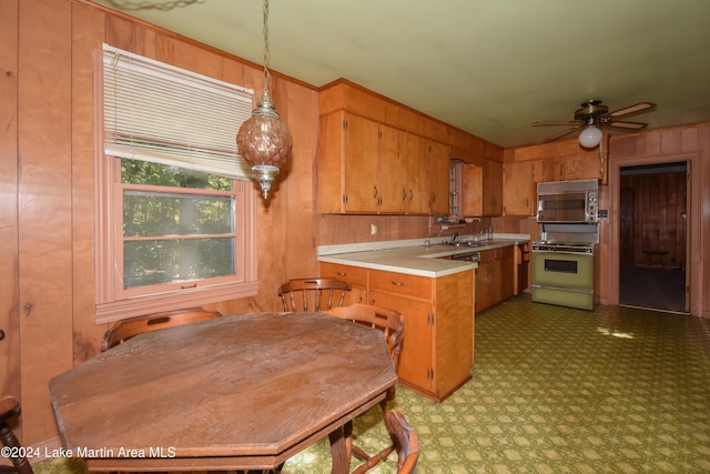 kitchen featuring ceiling fan, sink, hanging light fixtures, wood walls, and range with gas stovetop