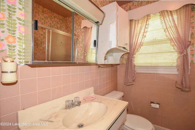 bathroom with vanity, toilet, tile walls, and walk in shower