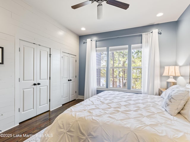 bedroom with multiple closets, dark hardwood / wood-style flooring, ceiling fan, and wood walls