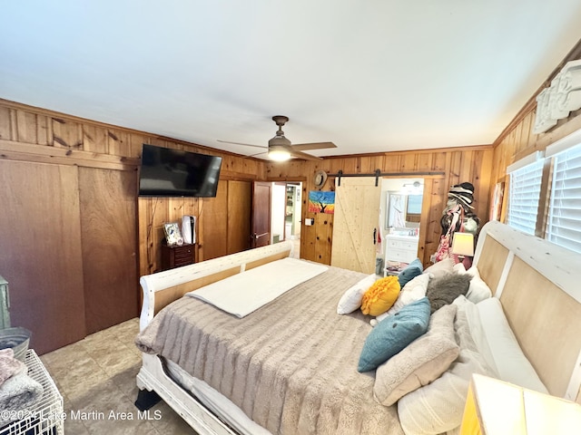 bedroom with a barn door, ceiling fan, wooden walls, and ornamental molding