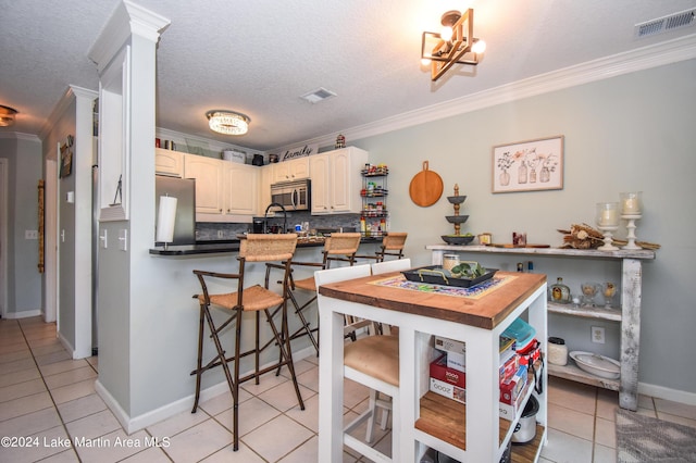 kitchen with backsplash, kitchen peninsula, crown molding, light tile patterned floors, and appliances with stainless steel finishes