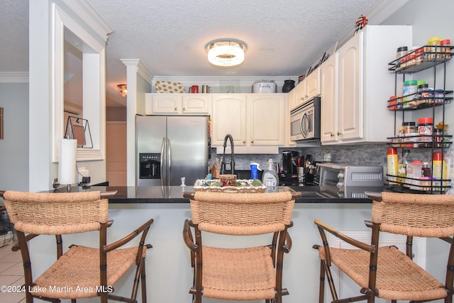 kitchen with kitchen peninsula, ornamental molding, appliances with stainless steel finishes, white cabinetry, and a breakfast bar area