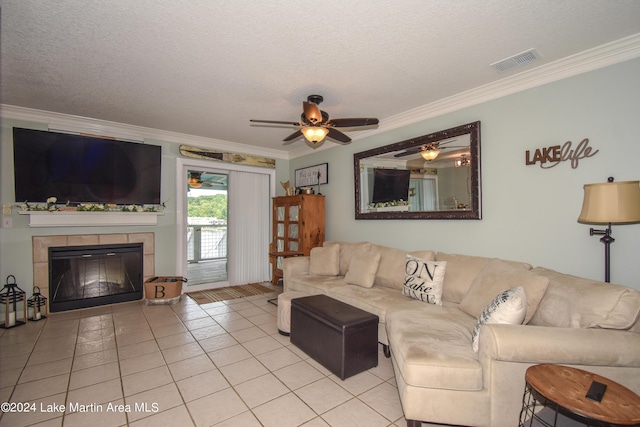 living room featuring ceiling fan, a textured ceiling, a fireplace, light tile patterned flooring, and ornamental molding