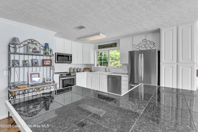 195 Honeysuckle Hl, Tallassee, AL 36078 - kitchen with stainless steel appliances, tile countertops, white cabinetry, a textured ceiling, and crown molding