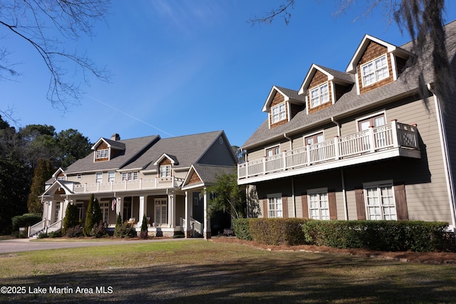 view of front of house featuring a porch, a chimney, a balcony, and a front yard