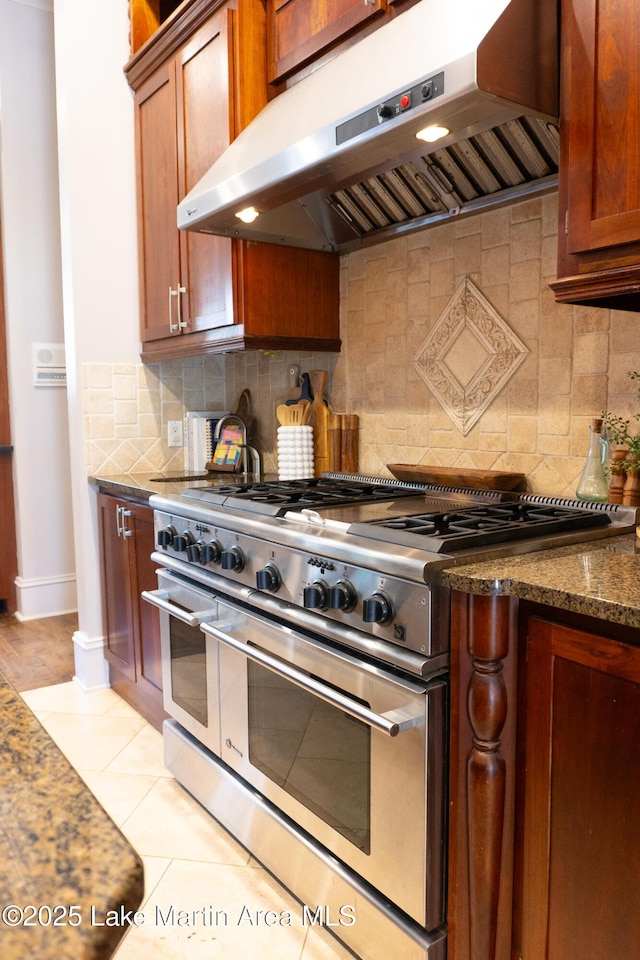 kitchen featuring dark stone counters, decorative backsplash, under cabinet range hood, and double oven range