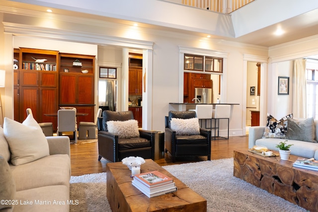 living area with ornamental molding, wood finished floors, and a towering ceiling