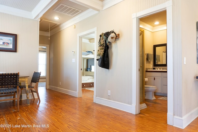 hallway featuring crown molding, visible vents, baseboards, a sink, and light wood-style flooring