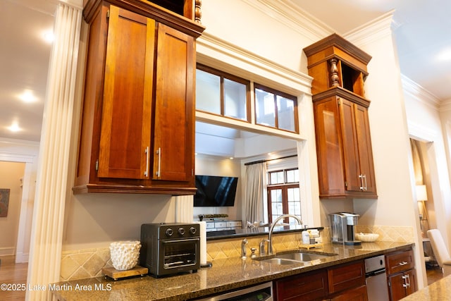 kitchen featuring crown molding, a toaster, dark stone counters, brown cabinets, and a sink