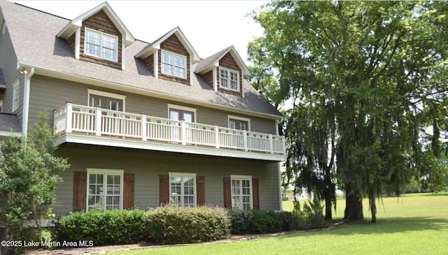 view of front facade featuring a balcony, a shingled roof, and a front yard