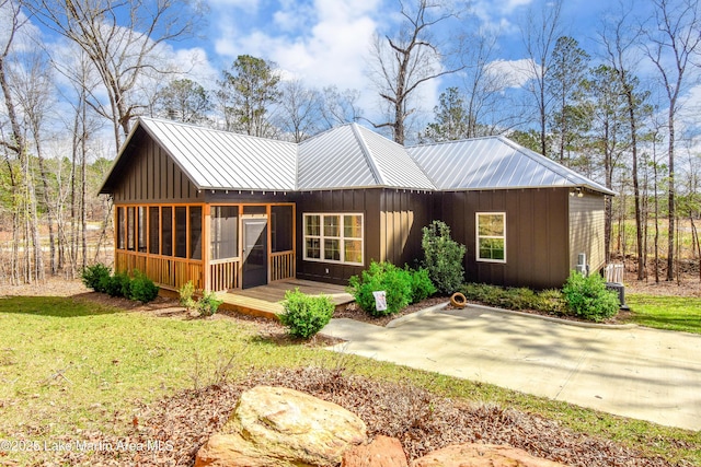 back of house featuring a sunroom, board and batten siding, metal roof, and a lawn