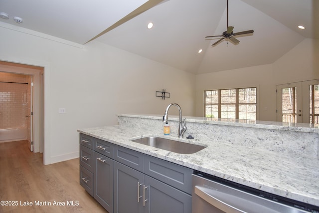 kitchen with a sink, light wood-type flooring, gray cabinetry, vaulted ceiling, and stainless steel dishwasher