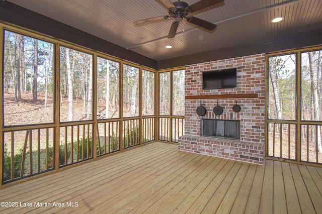 unfurnished sunroom with ceiling fan and a brick fireplace