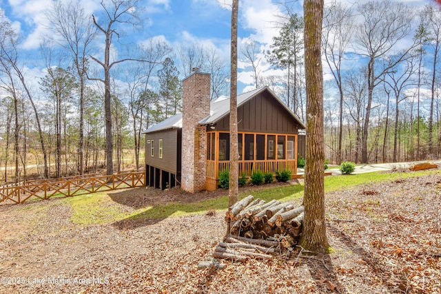 exterior space featuring a chimney, board and batten siding, a sunroom, metal roof, and fence