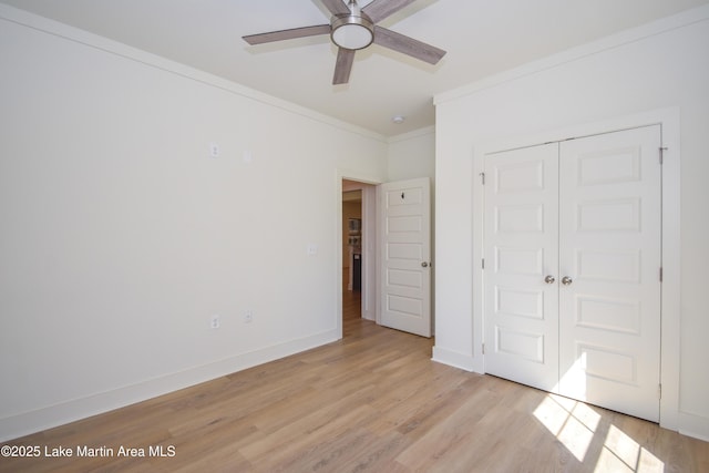 unfurnished bedroom featuring a closet, baseboards, ceiling fan, light wood-style floors, and crown molding