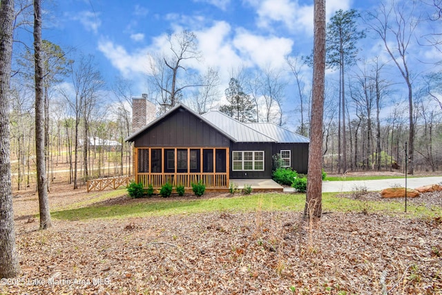 back of property with a sunroom, board and batten siding, and a chimney