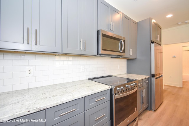 kitchen featuring light wood-style flooring, appliances with stainless steel finishes, light stone counters, decorative backsplash, and gray cabinetry