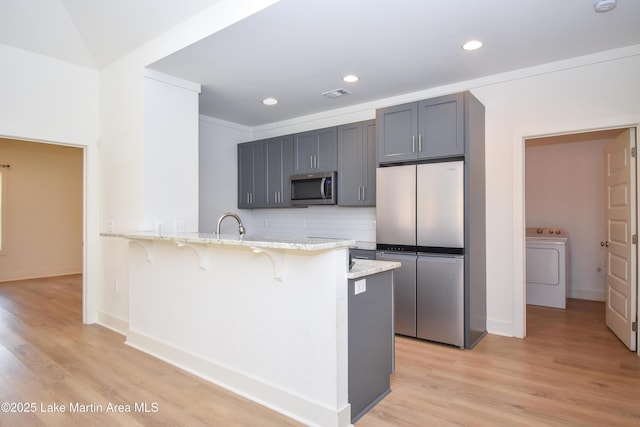 kitchen featuring a kitchen breakfast bar, washer / clothes dryer, a peninsula, appliances with stainless steel finishes, and light stone counters