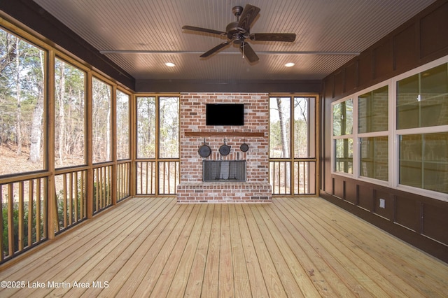 unfurnished sunroom featuring ceiling fan and a brick fireplace