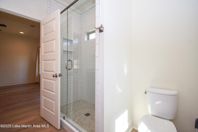 bathroom featuring toilet, a stall shower, wood finished floors, and baseboards