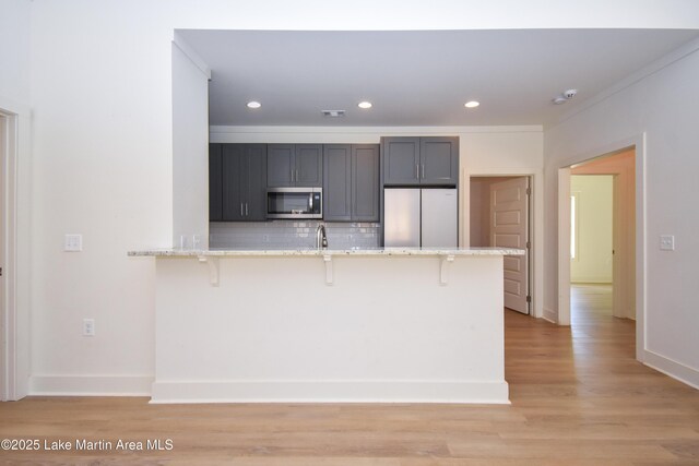 kitchen with a kitchen bar, tasteful backsplash, light wood finished floors, and stainless steel appliances