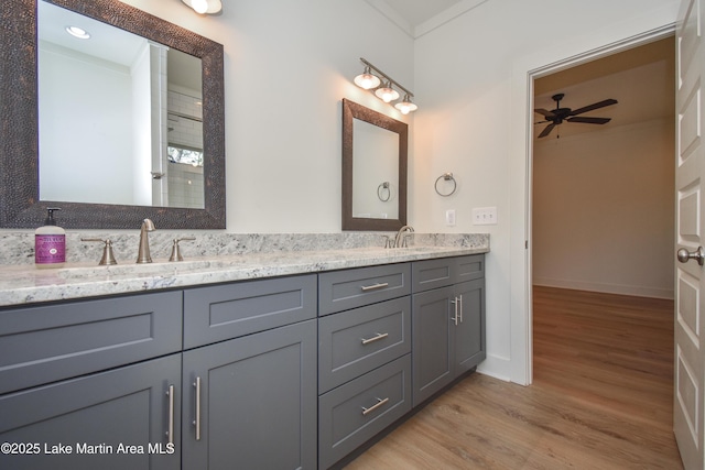 full bath featuring baseboards, a sink, a ceiling fan, double vanity, and wood finished floors