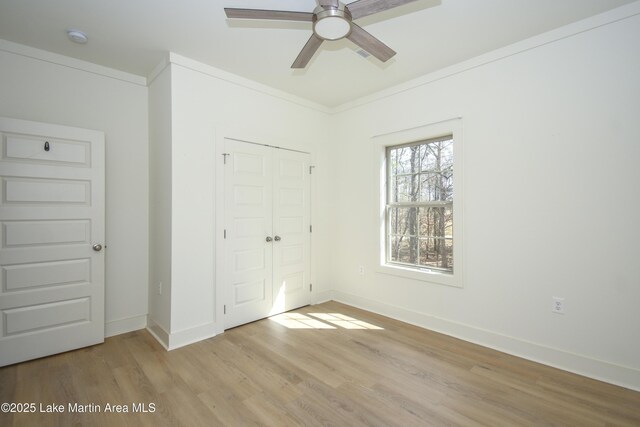 unfurnished bedroom featuring light wood-style floors, a closet, crown molding, and baseboards