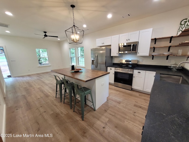 kitchen with wooden counters, stainless steel appliances, open shelves, visible vents, and a sink