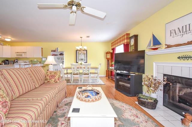 living room with light wood-type flooring, a tiled fireplace, and ceiling fan with notable chandelier