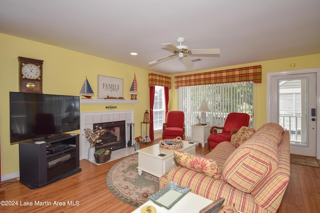 living room with ceiling fan, a tiled fireplace, and hardwood / wood-style flooring