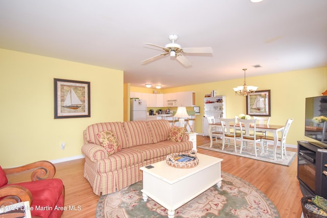 living room with ceiling fan with notable chandelier and light hardwood / wood-style flooring