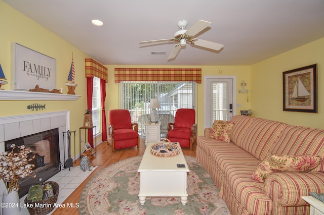 living room with light hardwood / wood-style floors, a tile fireplace, and ceiling fan