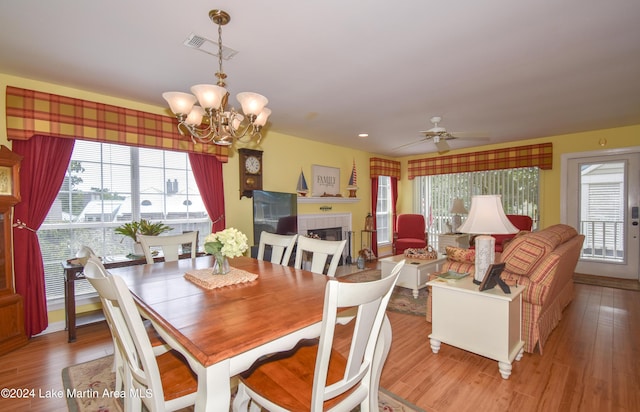 dining room with a tiled fireplace, ceiling fan with notable chandelier, and hardwood / wood-style flooring