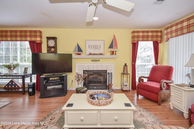 living room with light wood-type flooring, a tiled fireplace, and ceiling fan