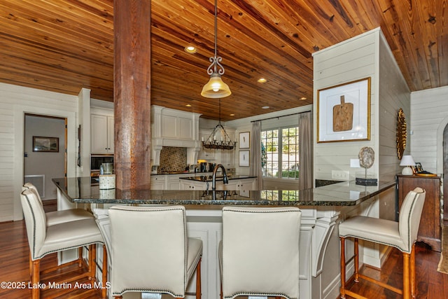 kitchen with dark wood-type flooring, a breakfast bar area, hanging light fixtures, wooden ceiling, and white cabinets