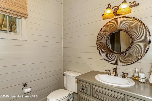 bathroom featuring vanity, wooden walls, and toilet