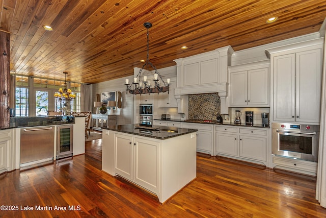 kitchen featuring an inviting chandelier, decorative light fixtures, dark stone countertops, appliances with stainless steel finishes, and beverage cooler