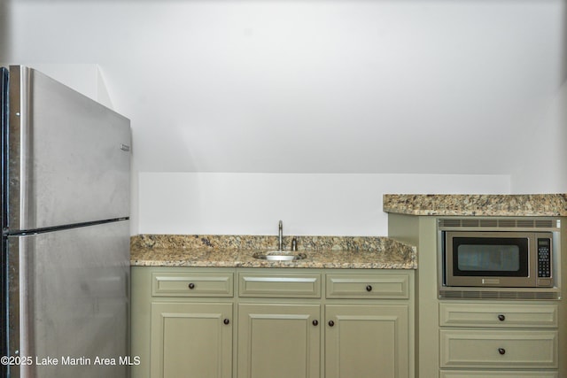 kitchen with light stone counters, stainless steel appliances, vaulted ceiling, and sink