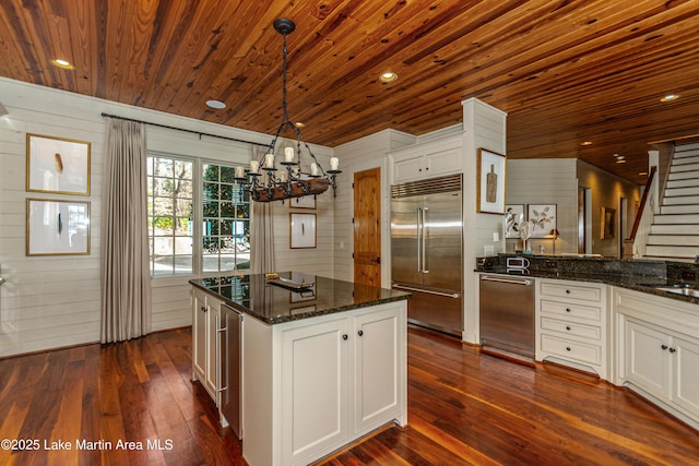 kitchen featuring appliances with stainless steel finishes, white cabinetry, dark stone countertops, a kitchen island, and wooden ceiling