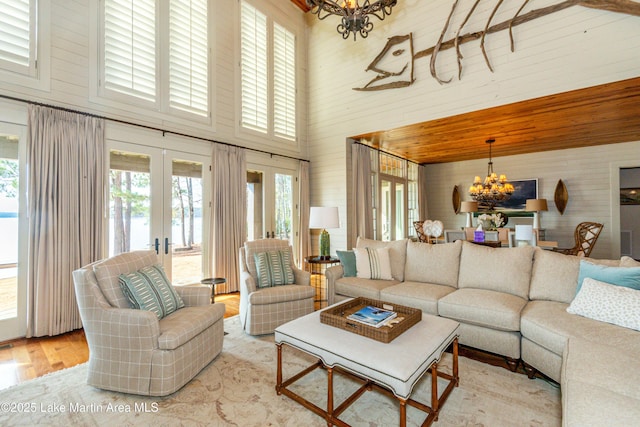 living room featuring french doors, wood walls, a chandelier, light hardwood / wood-style flooring, and a towering ceiling